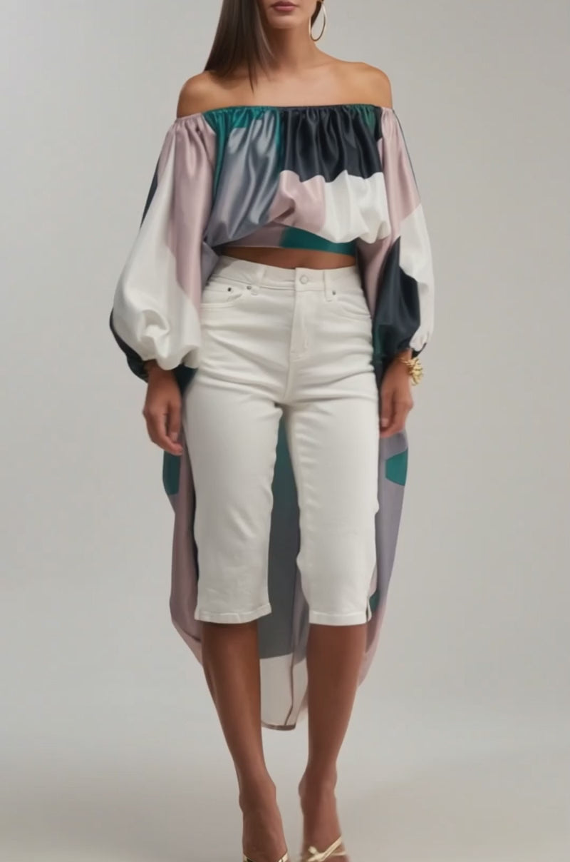 A video of a woman wearing the BE WITH ME BLOUSE IN GREEN MULTI with oversized sleeves, paired with white knee-length pants and gold heeled sandals.
