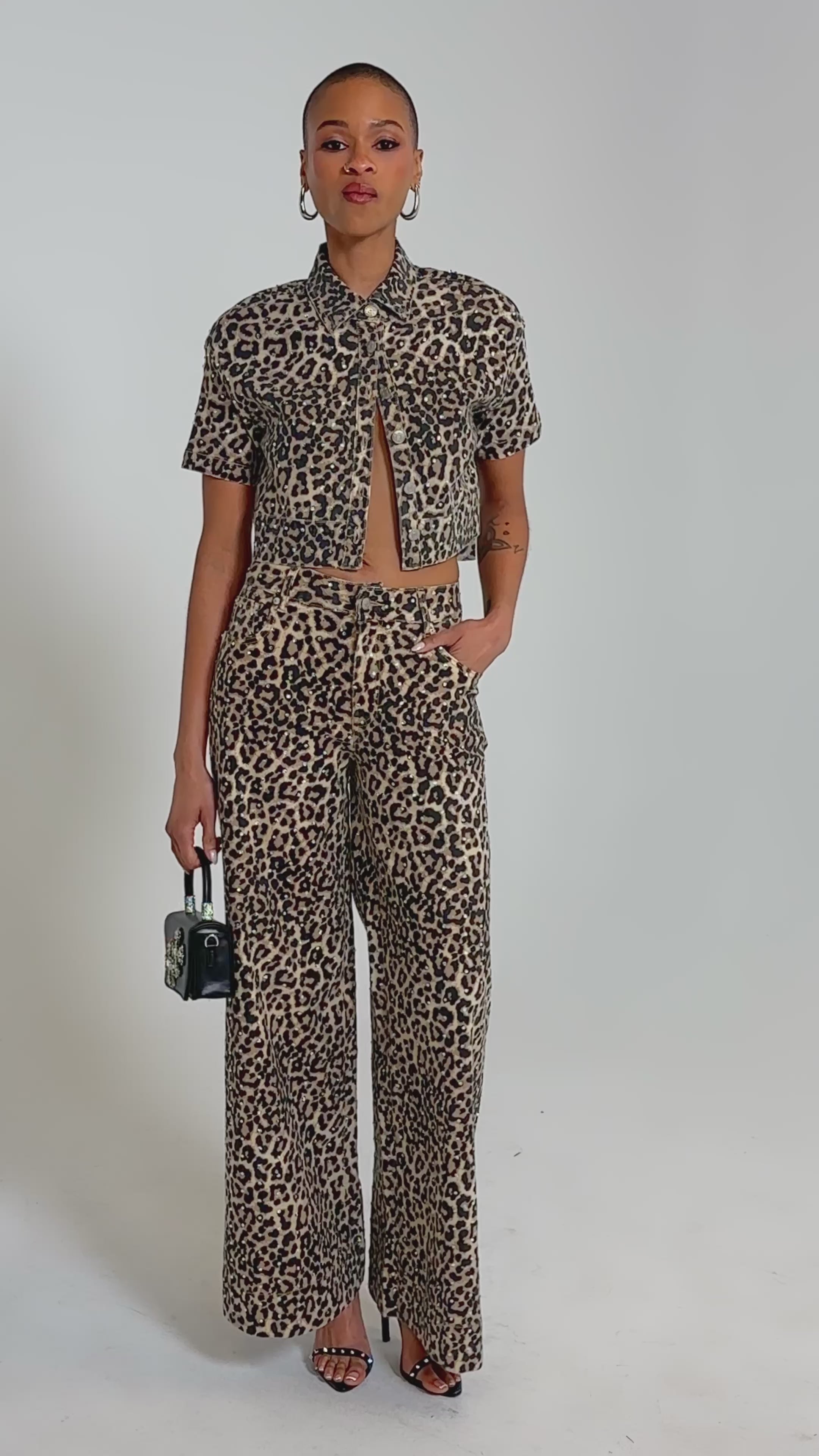 Video of woman modeling the LEOPARD SISTA RELAXED DENIM jeans and a matching leopard print short-sleeve shirt, accessorized with hoop earrings, strappy sandals, and a small black handbag.