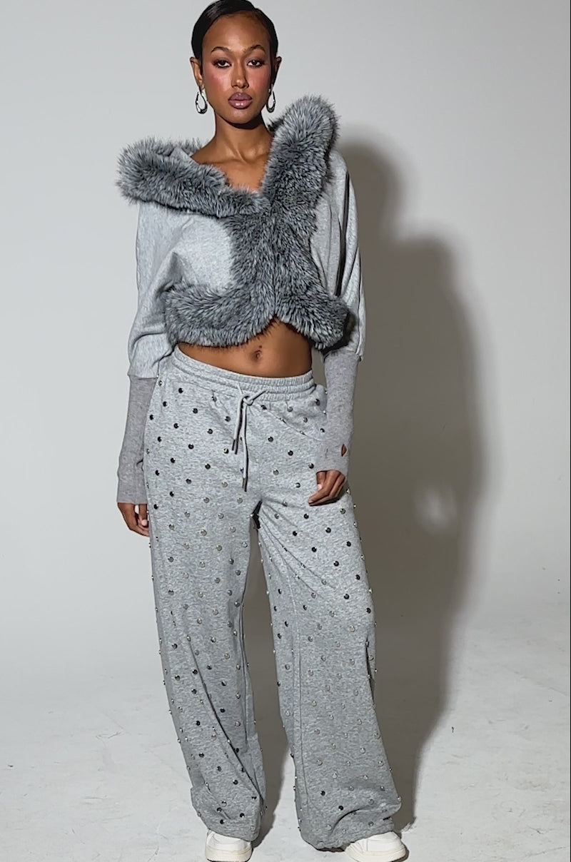 Video of woman modeling the MOVIN DIFFERENT SWEATSHIRT WITH FUR TRIM in light gray, paired with matching studded gray pants. The sweatshirt features a thick faux fur-edged hood 
