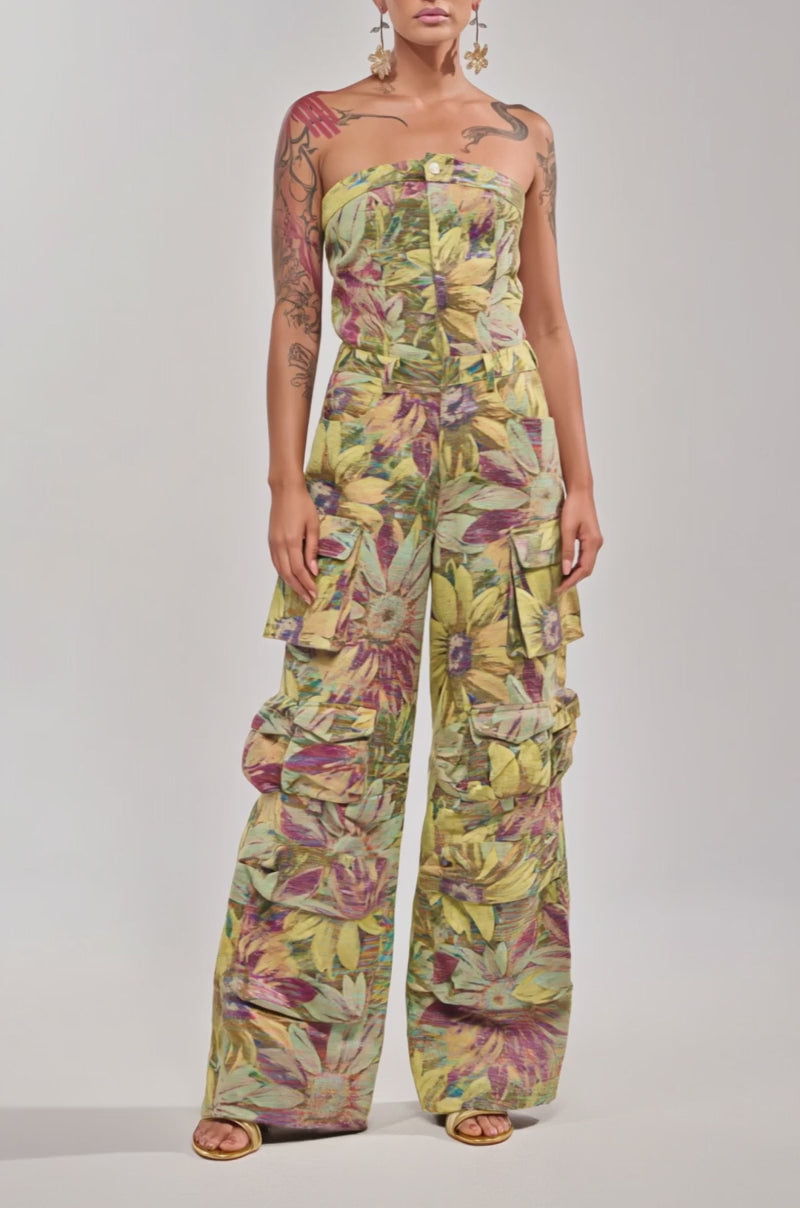A video of a woman in the SMELL THE FLOWERS BROCADE STRAPLESS JUMPSUIT, featuring a multicolored leafy floral print. 