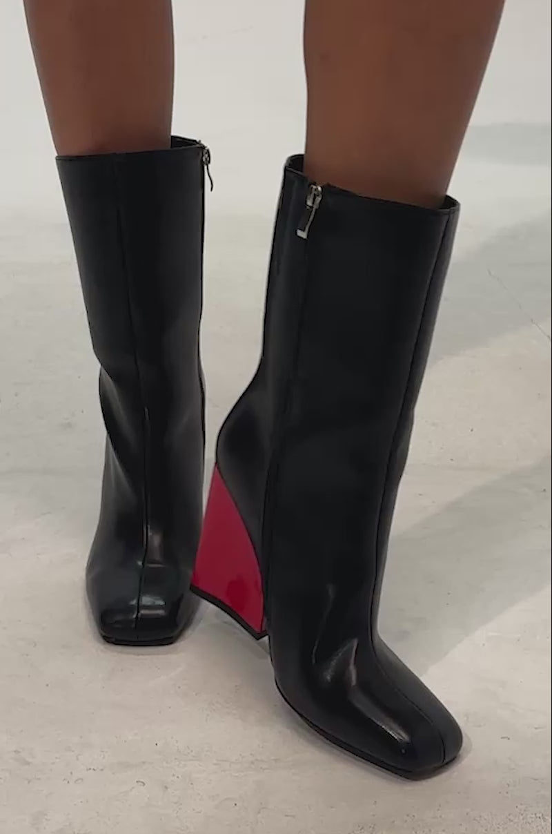 Video of woman modeling the AZALEA WANG NOTEBOOK BLACK BOOT, featuring faux leather material and shiny red block heels, shown against a plain light background.