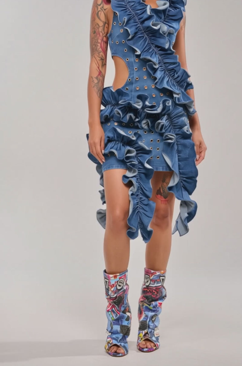 A video of a woman in the LINGERING EYES FLOCKED DENIM MINI DRESS, featuring ruffles and grommets, paired with colorful knee-high boots. 
