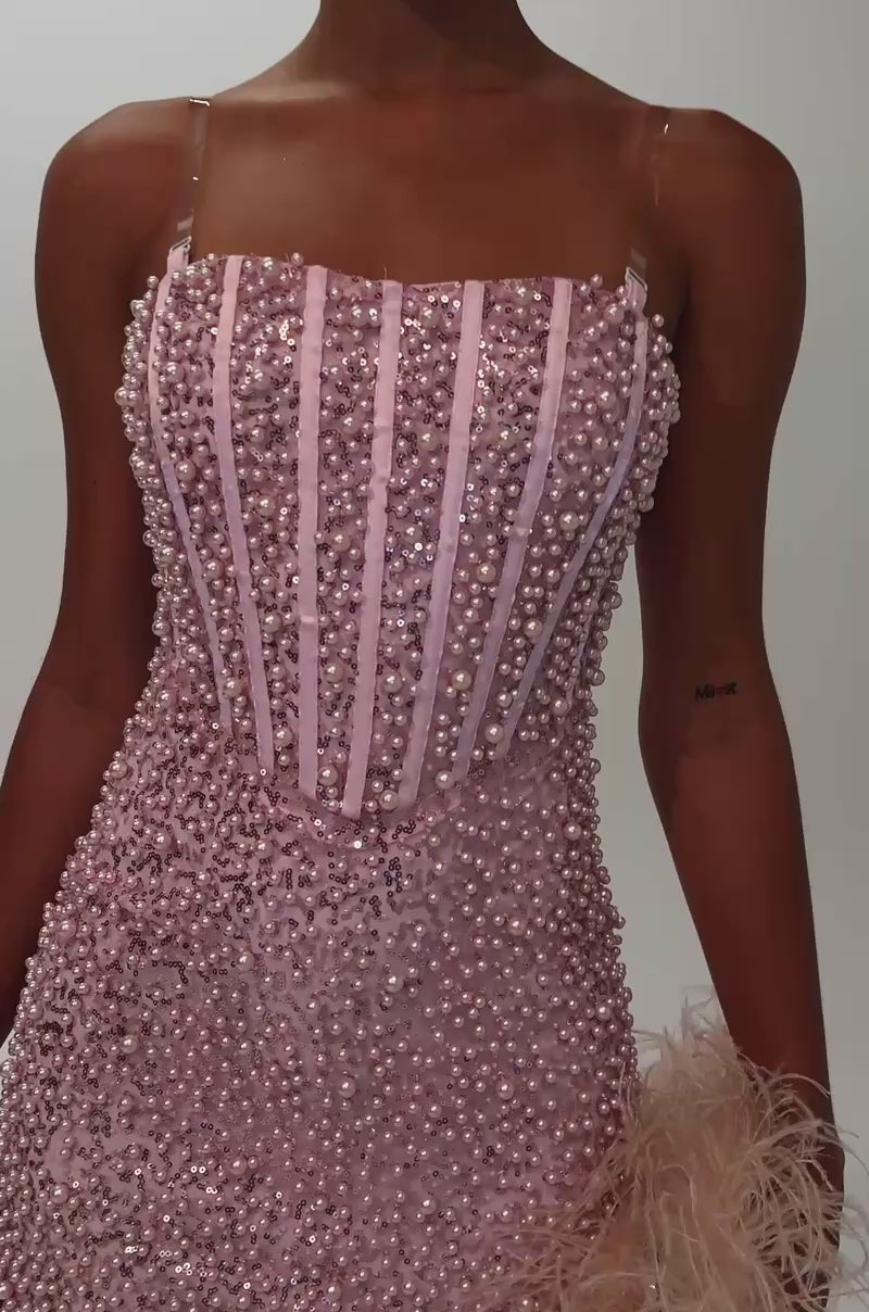 Video of woman modeling the PEARLS FOR THE GIRLS MINI DRESS IN PINK, a fitted mini dress with textured beads, vertical stripes, thin straps. She accessorizes with hoop earrings and carries a beige feathered clutch.