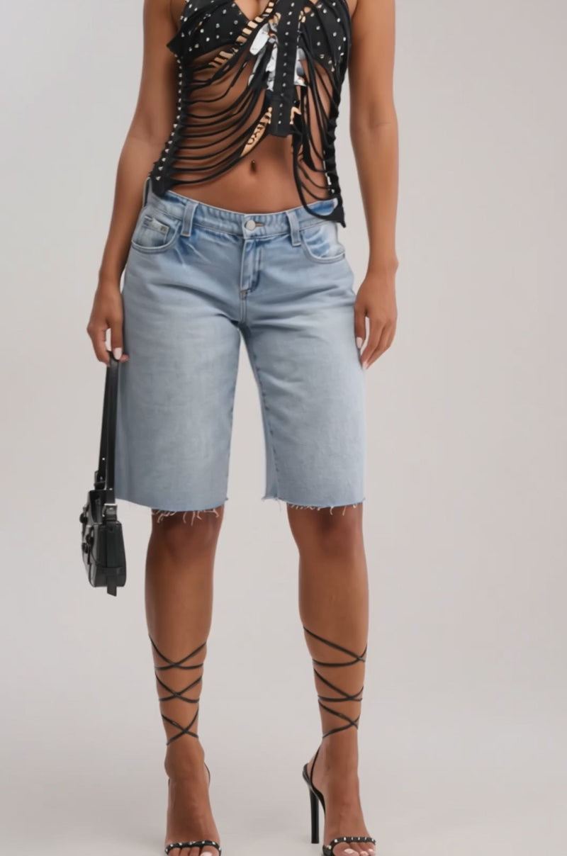 Video of woman modeling the ULTRA LOW RISE DENIM BERMUDA SHORTS styled as streetwear, paired with a black strappy top, high-heeled sandals, and a small black handbag. 