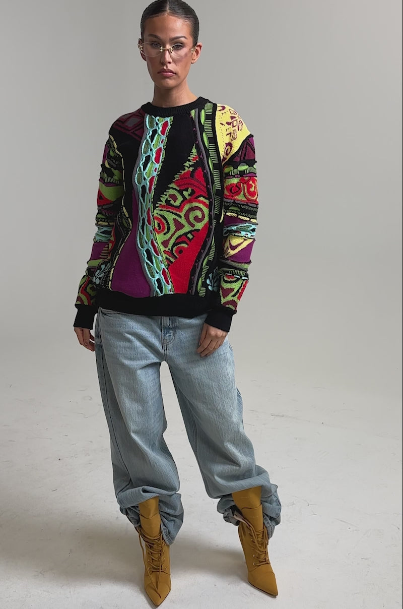 Video of woman modeling the GET GROOVY SWEATER—an oversized vintage piece with red, green, blue, and purple designs—and clear glasses 