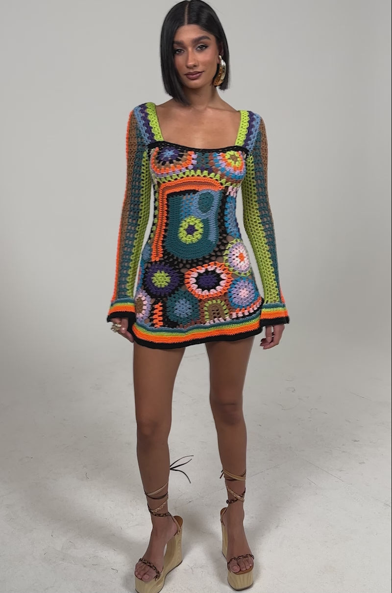 Video of woman modeling the PARADISE FOUND KNIT MINI DRESS, a colorful boho-chic mini dress with bright geometric crochet patterns, standing against a plain light background.