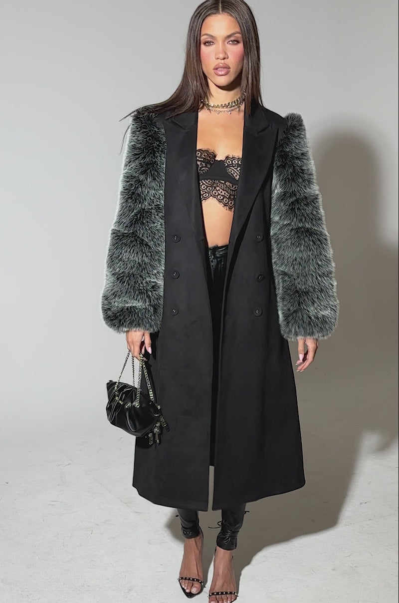 Video of woman modeling the NOLITA FUR SLEEVE TRENCH, a long black coat with gray fur sleeves, layered over a black lace bralette and pants