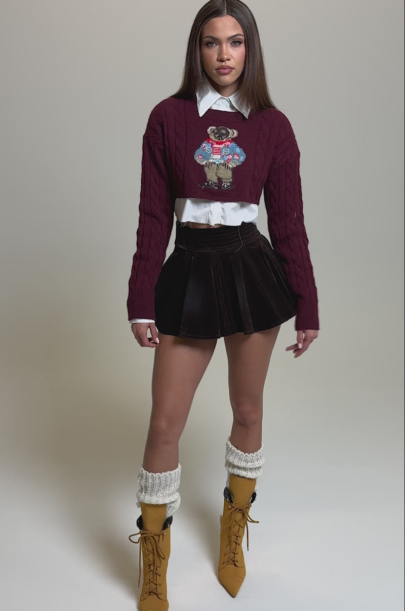 Video of woman modeling the CALL ME VELVET MINI SKIRT in dark brown. The skirt features a high waist and pleated A-line silhouette. Their hands are relaxed at their sides.