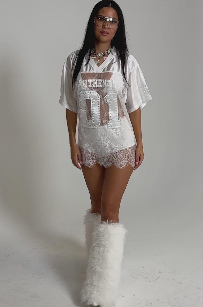 A video of a woman wearing oversized sunglasses, layered necklaces, and the CHARMING LACE JERSEY DRESS—an oversized, relaxed fit with "01 AUTHENTIC" on the front.