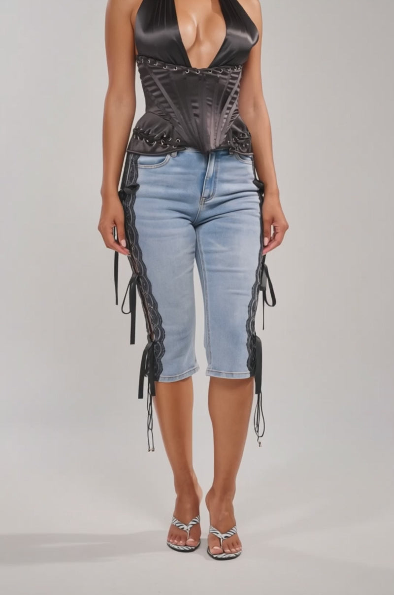 A video of a woman in the NOT MY PROBLEM SATIN CORSET, styled with light blue knee-length jeans featuring black lace-up details.