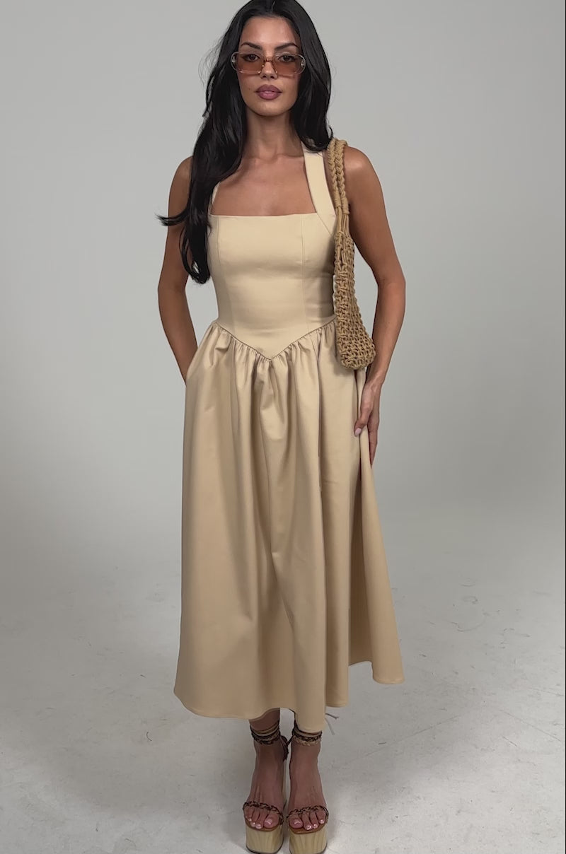 Video of woman modeling the SWEET SOFIE HALTER MIDI DRESS, featuring a khaki corset-inspired bodice and gathered skirt. She accessorizes with sunglasses, wedge sandals, and a woven bag over her shoulder against a light background.