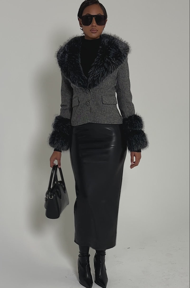 Video of woman modeling the I SEE LONDON FUR TRIM BLAZER with faux fur collar and cuffs, a black turtleneck, and leather skirt posing confidently holding a black handbag against a plain background.