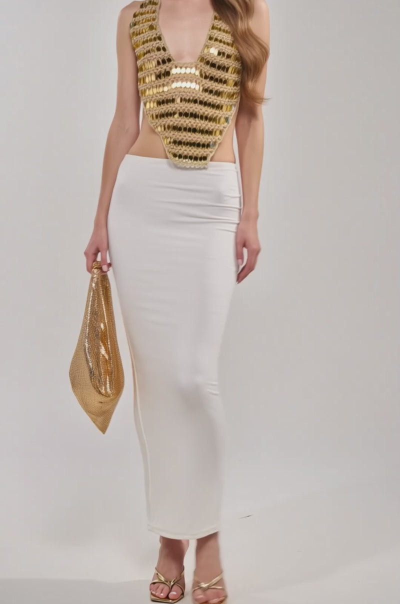 Video of woman modeling the GOLDEN GIRL CROCHET SEQUIN TOP, featuring a gold metallic crochet design, deep neckline, and open back. She pairs it with a white skirt and poses confidently against a plain light background.