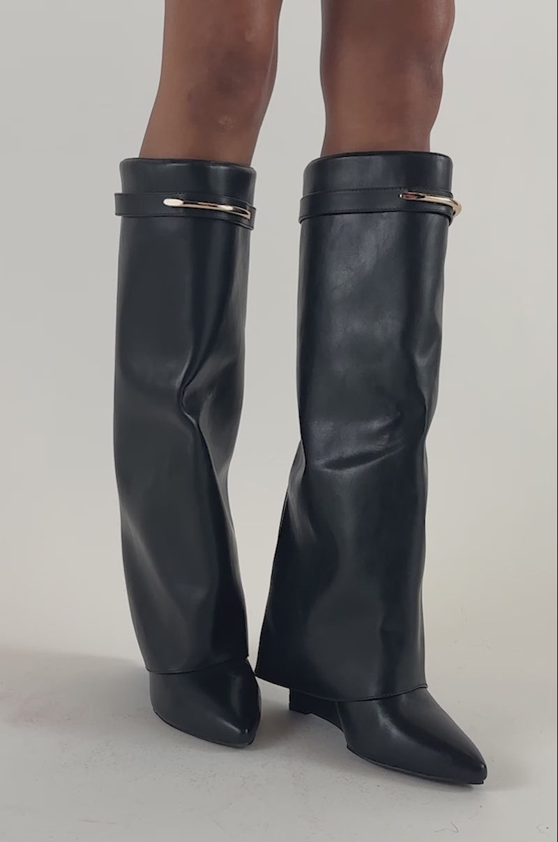 Video of a woman modeling the AZALEA WANG LOVE BURN BLACK SHARK WEDGE BOOT, featuring tall, slouchy black faux leather with subtle gold hardware.