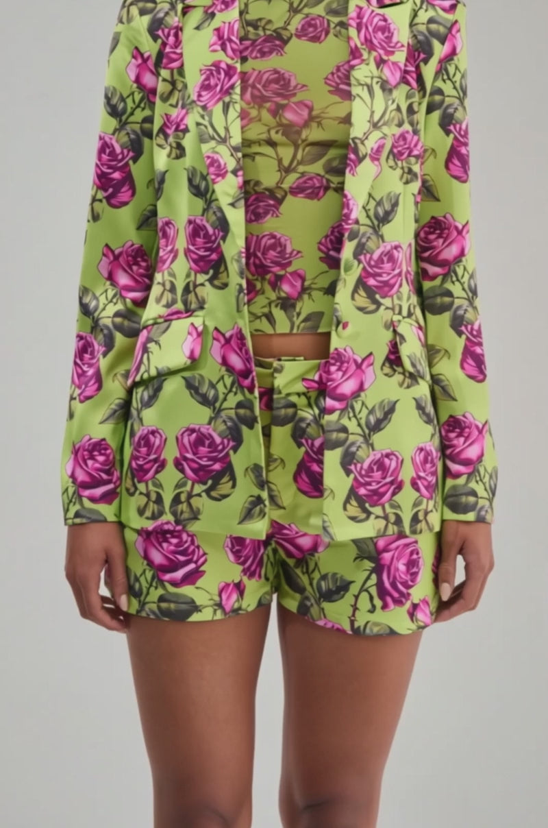 Video of a woman modeling the DOZEN ROSES SATIN BLAZER IN CHARTREUSE with matching high-waisted shorts and a sheer floral turtleneck.