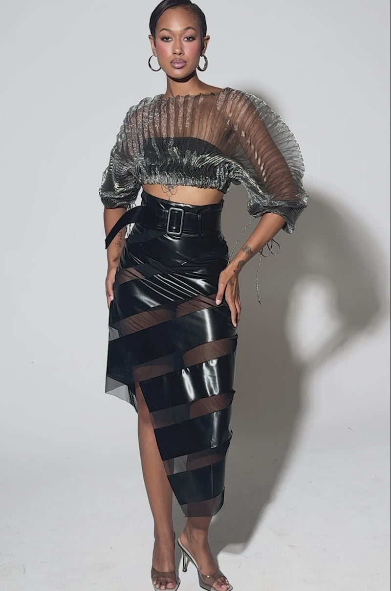 Video of woman modeling the SHEER PLEATED CROP TOP IN GREY, and high-waisted black vinyl pants with a big belt.