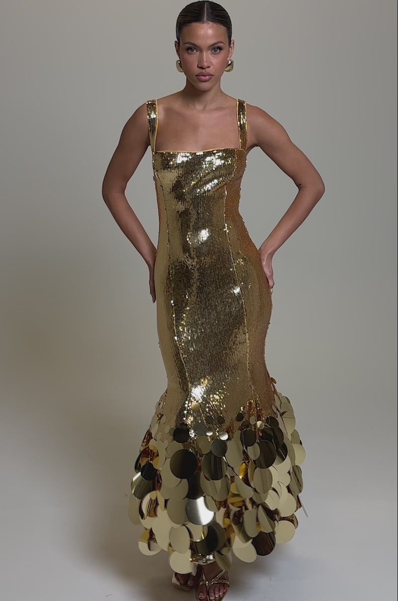 Video of woman modeling the LIFE OF THE PARTY SEQUIN MIDI DRESS—a form-fitting gold sequin piece with large shiny discs at the hem. She completes her look with gold heels and earrings, posing confidently against a neutral backdrop.
