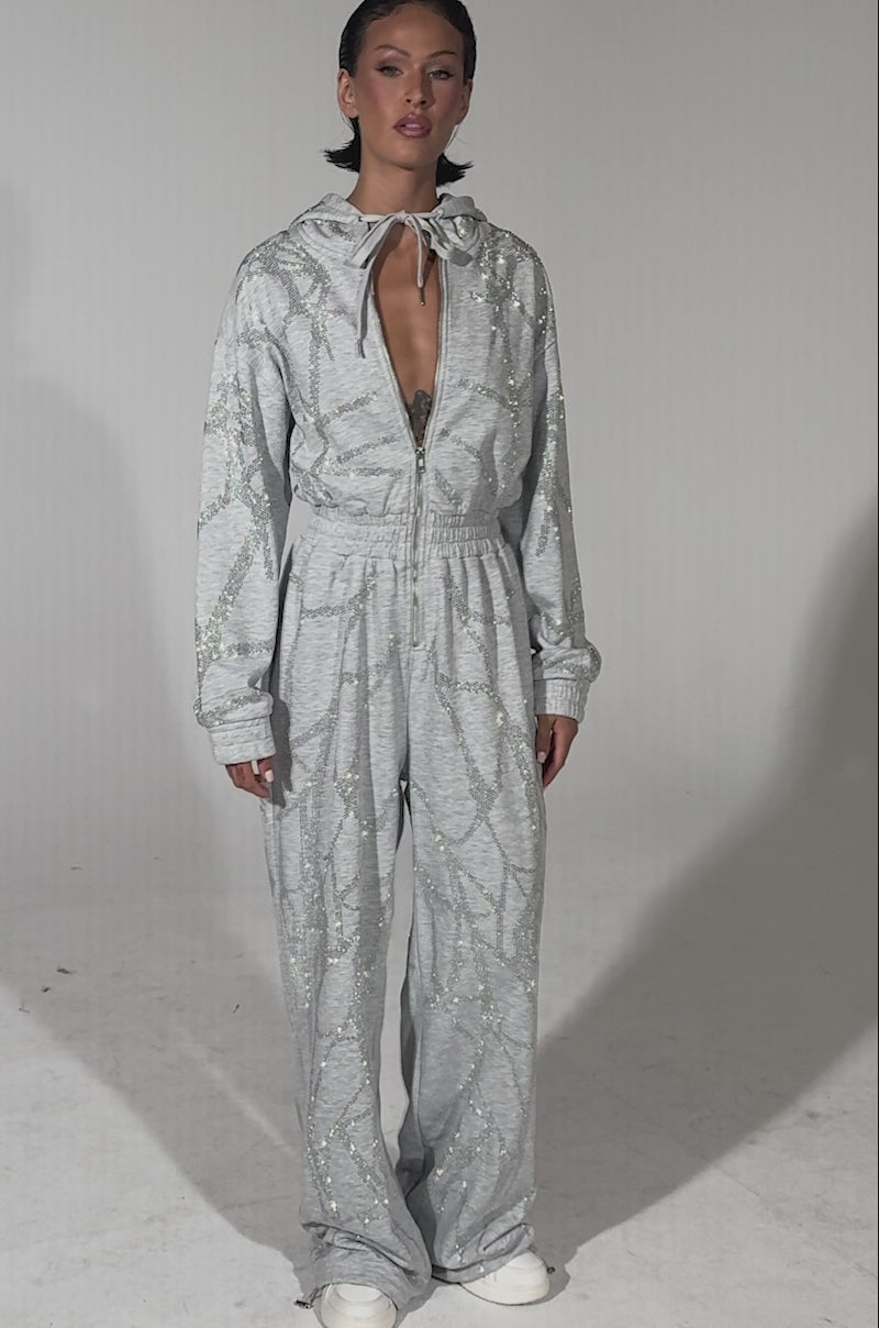 A video of a woman wearing the NEVER BUGGIN PRINTED FRENCH TERRY JUMPSUIT, a grey loungewear piece.
