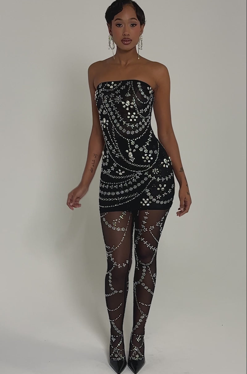 Video of woman modeling the JEWELED UP TWO-PIECE RHINESTONE MINI DRESS, paired with sparkling sheer tights and strappy heels. Her hair is slicked back, highlighting the outfit’s radiant rhinestone details.