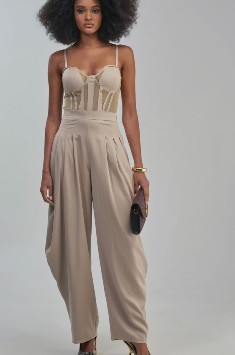 Video of a woman modeling the NO FUNNY BUSINESS CORSET JUMPSUIT, which features a flattering sweetheart neckline, dramatic balloon pant legs, and a chic khaki hue. 