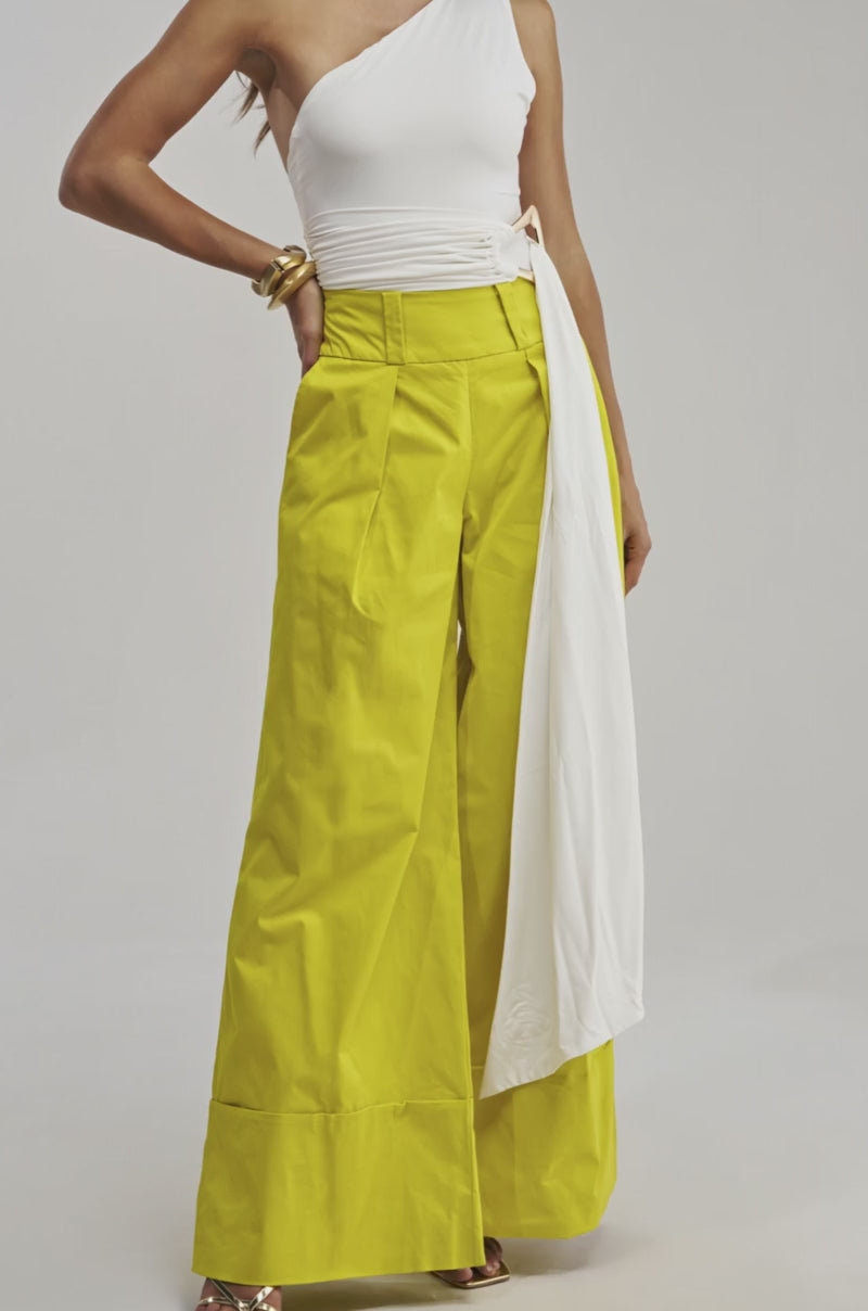 Video of a woman modeling the FEELING GOOD BODYSUIT WITH BELT, a chic white one-shouldered bodysuit featuring a long sash, paired with wide-leg, high-waisted yellow pants.