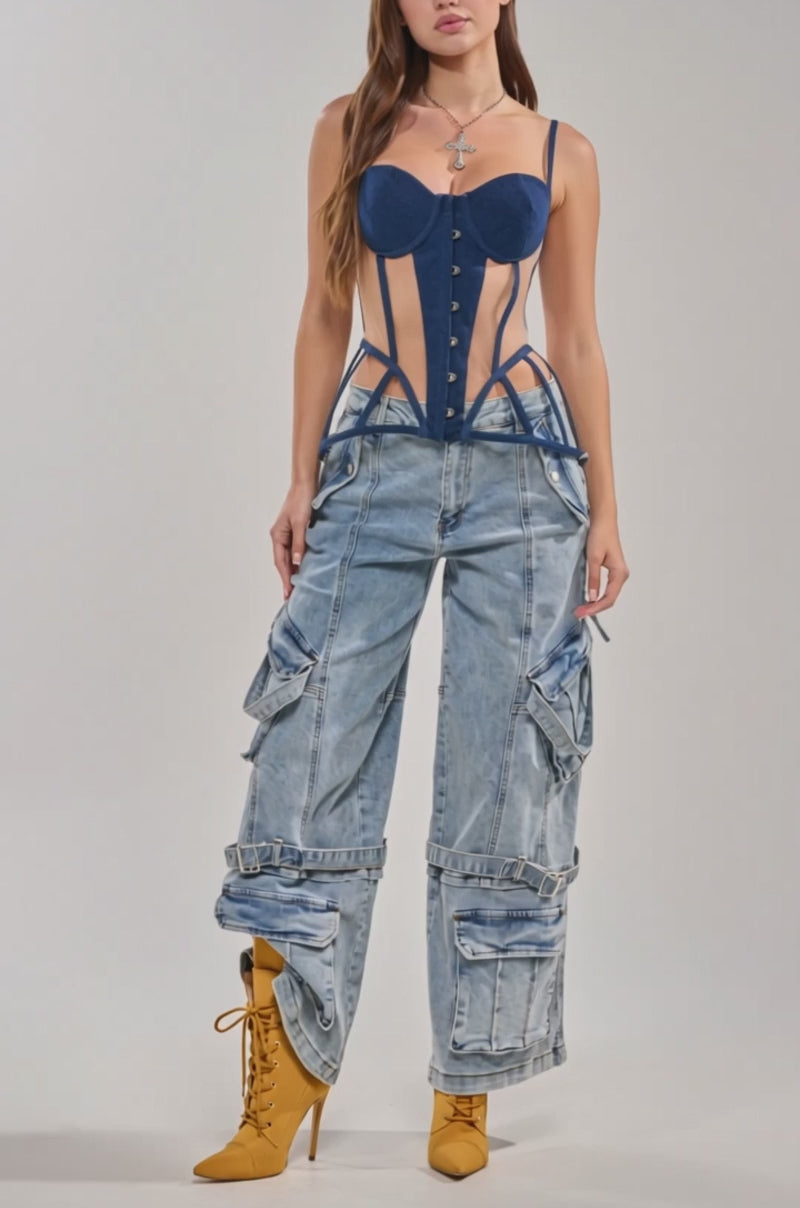 Video of woman modeling the TOO HOT FOR YOU CORSET—a blue denim peplum corset top with side cutouts and wide straps—paired with light blue baggy jeans with pockets and ties. She has long brown hair, a necklace, and stands against a plain background.