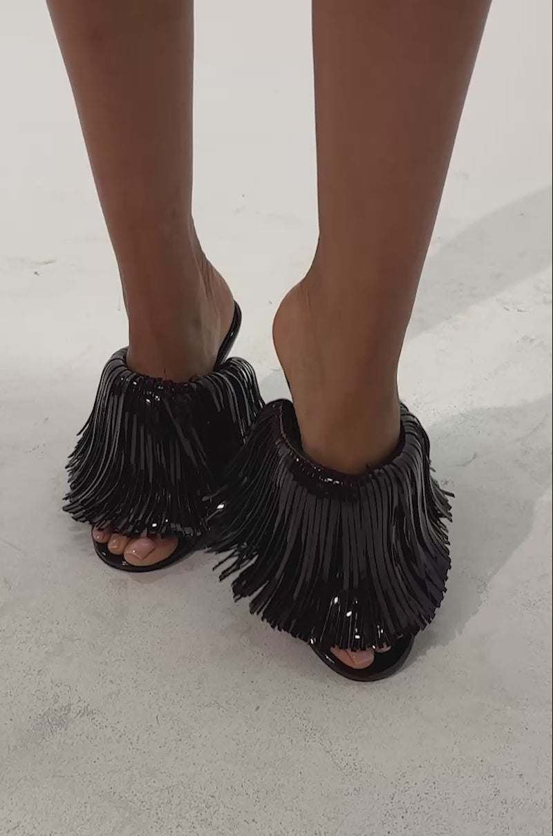 Video of a woman modeling the AZALEA WANG VAILYN PURPLE PATENT FRINGE PU WEDGE SANDAL, featuring shiny long fringe details and a bold open-toe wedge design.