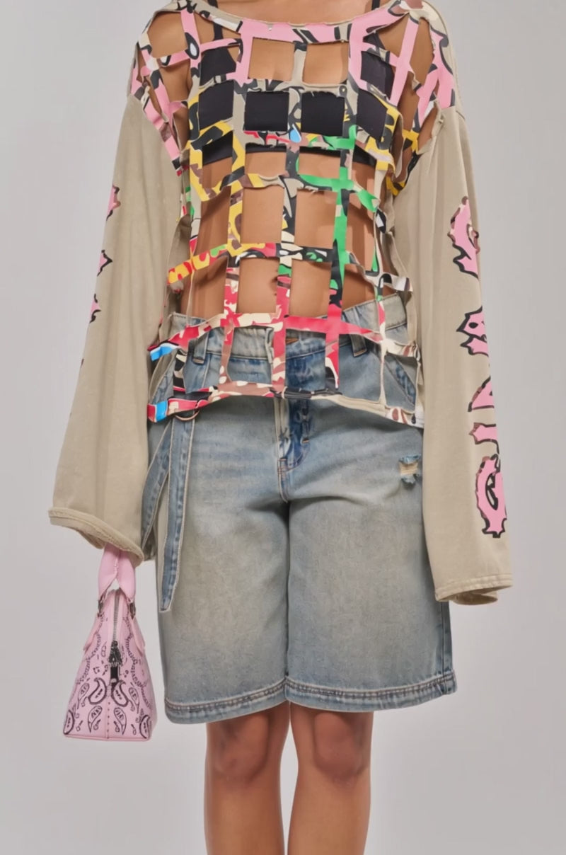 Video of woman modeling the CAGED UP LONG SLEEVE GRAPHIC TEE, holding a pink patterned handbag—streetwear layering perfection.