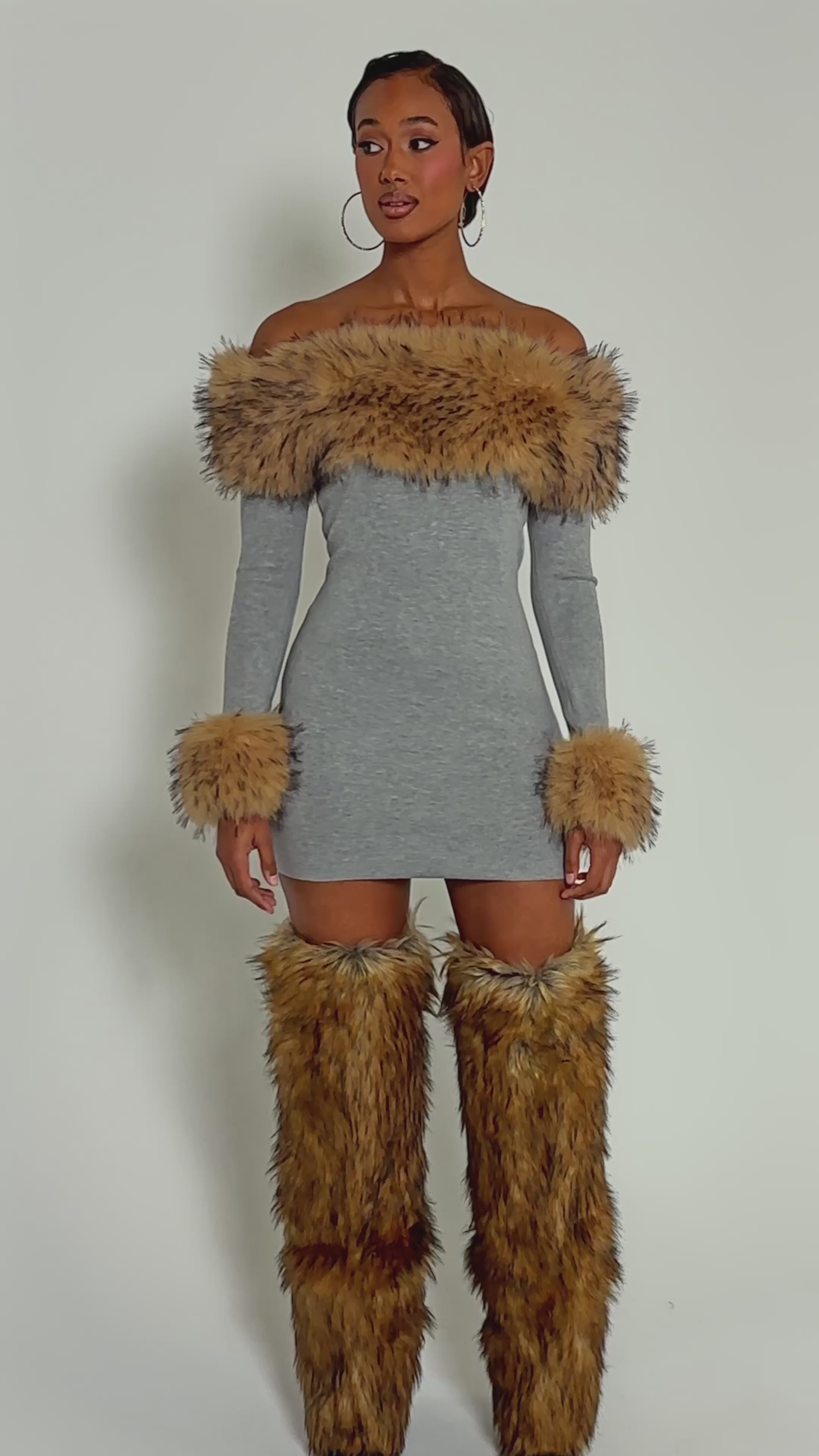 Video of woman modeling the COMFY COZY FUR TRIM MINI DRESS IN GREY, featuring a fitted ribbed knit, off-shoulder cut, and fur trim on the neckline and cuffs, paired with matching boots against a light background.