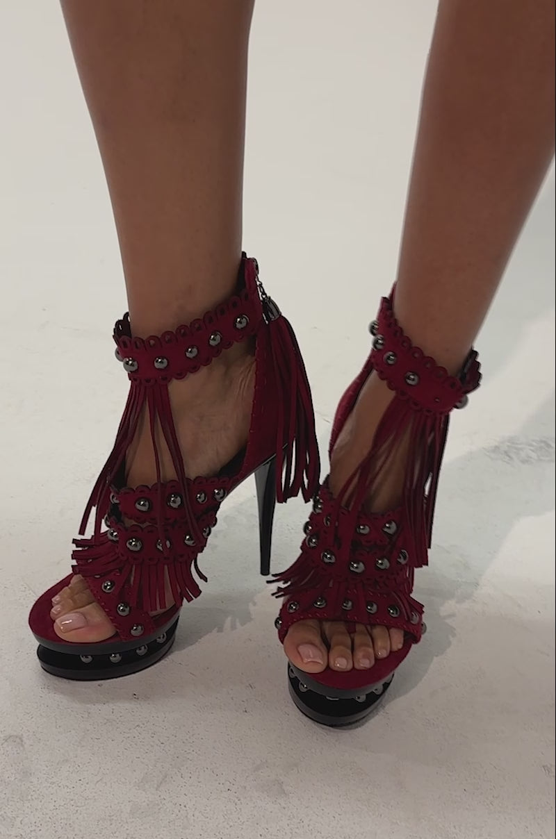 Video of a woman modeling the AKIRA GOLD BURGUNDY SUEDE STILETTO SANDAL—high-heeled, open-toe sandals in a rich burgundy suede with fringe and eyelet details, finished with bold black platform soles.