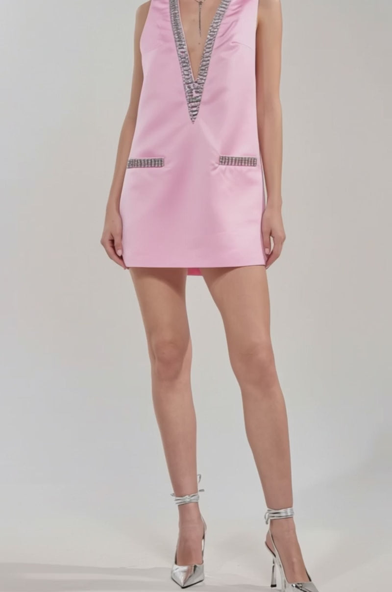 Video of woman modeling the UNDER THE LIGHTS SEQUIN MINI DRESS, a pink satin mini with a sleeveless shift silhouette, deep V-neckline, and sparkly rhinestone embellishments on the neckline and pocket flaps.