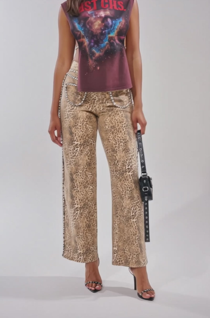 A video of a woman in the LAST CALL RHINESTONE EMBELLISHED GRAPHIC TANK, paired with beige leopard print wide-leg pants, black heeled sandals, and a studded crossbody bag. 