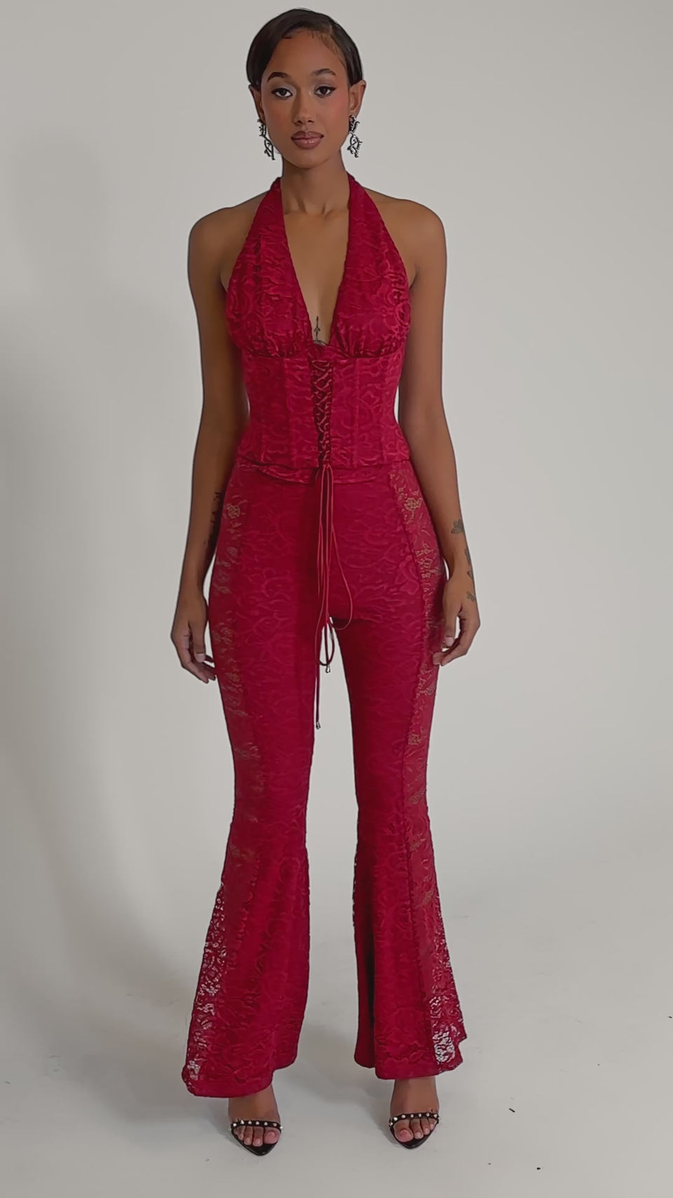 A video of a woman wearing the LOVE BOMB LACE CORSET, styled with fitted bodice, flared legs, and strappy high-heeled sandals.