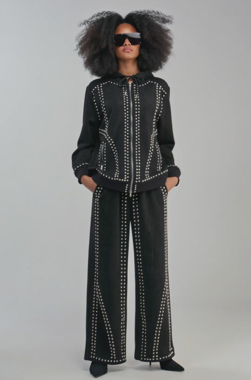 Video of a woman modeling the ASHLEY STUDDED ZIP UP SWEATSHIRT. The studded black sweatshirt is paired with matching silver-studded pants.