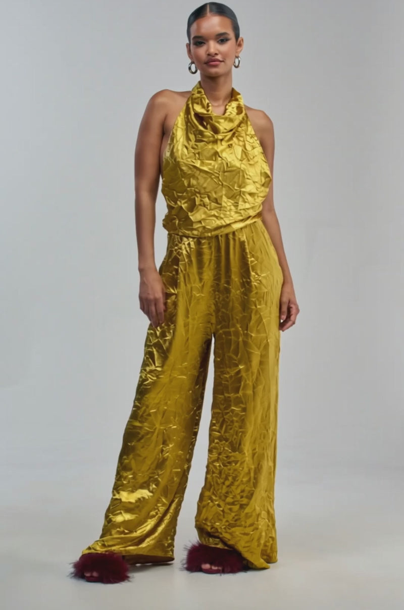 Video of a woman modeling the CALLING ALL THE GIRLS SATIN JUMPSUIT IN GOLDEN YELLOW—a shiny, halter-style jumpsuit with wide legs.