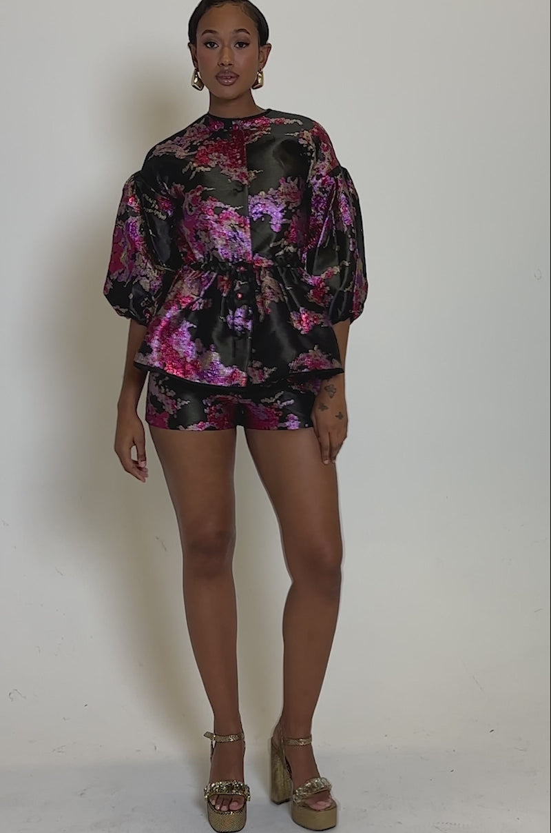 Video of woman modeling the ETHEREAL BROCADE SHORTS IN PINK—high-rise shorts with a vintage-inspired floral pattern in black, pink, purple, and gold. 