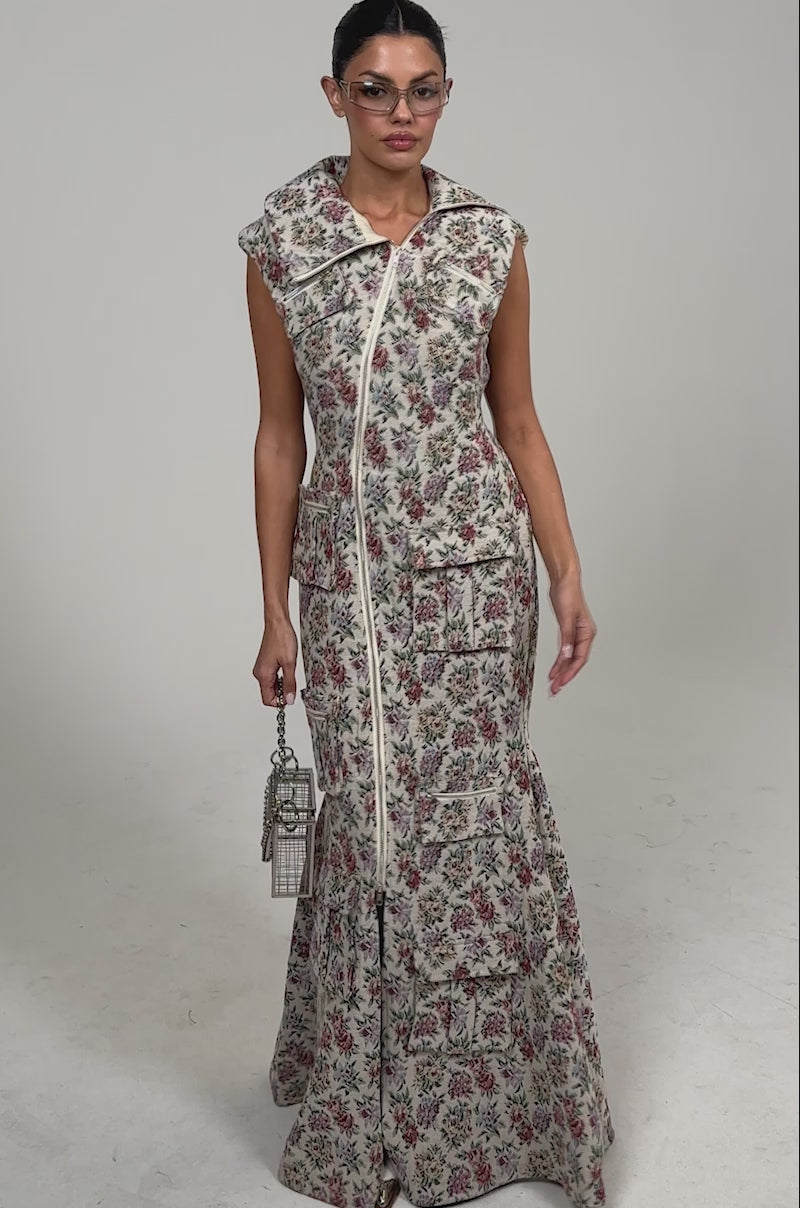 Video of woman modeling the FLOWER POWER TAPESTRY MAXI DRESS with a sleeveless design, high asymmetrical zip-up collar, and multiple large pockets