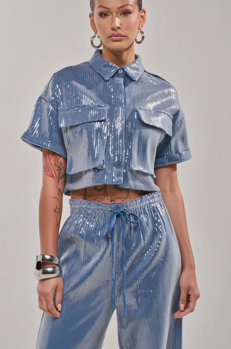 Video of woman modeling the SHAKE IT GIRL SEQUIN BUTTON DOWN in shiny blue, paired with matching pants. 