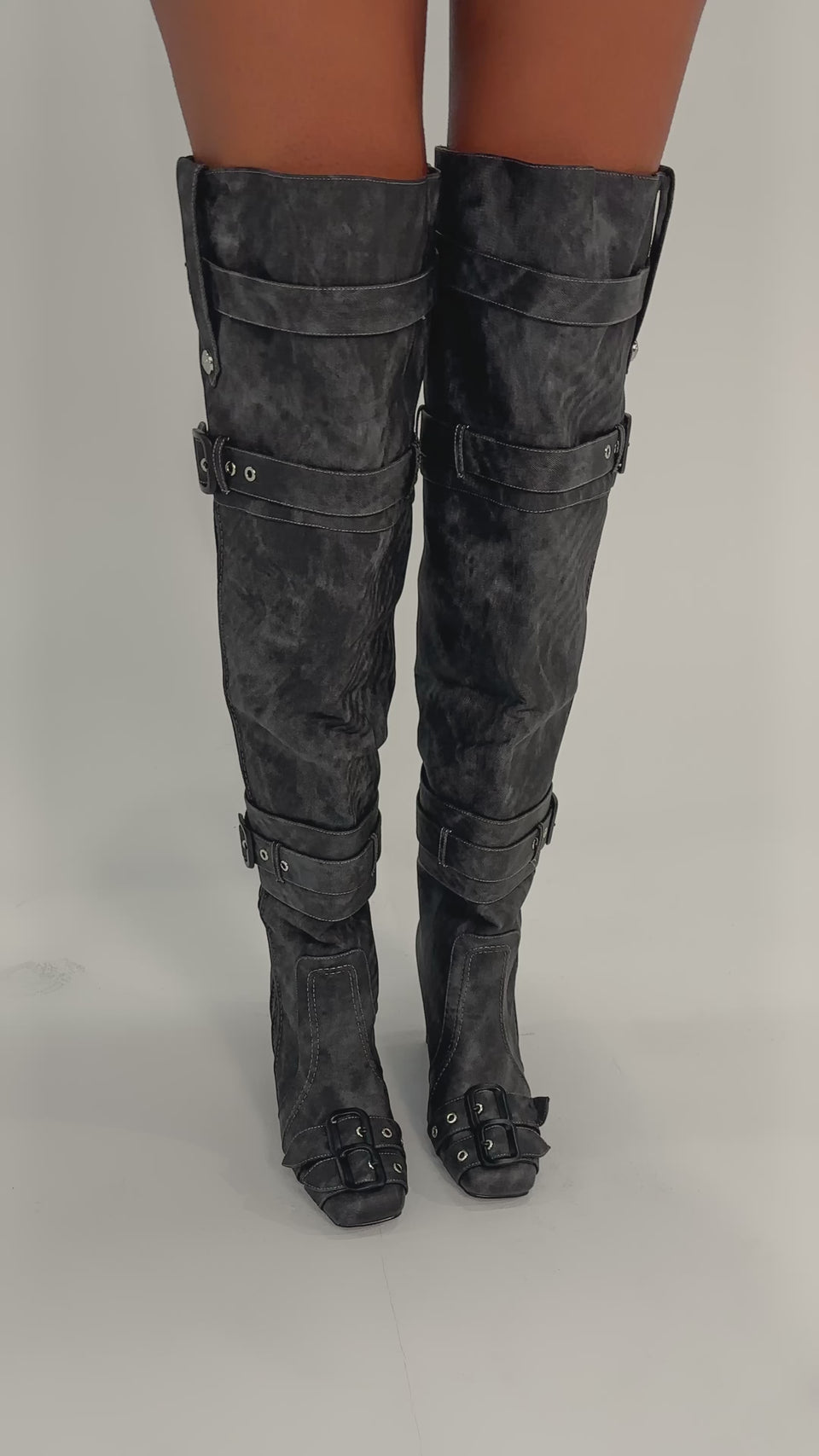 A video of a person wearing the AZALEA WANG TRILLION CHARCOAL CHUNKY THIGH HIGH BOOT, featuring black over-the-knee design with buckles and straps, standing on a plain light background to showcase its bold style.