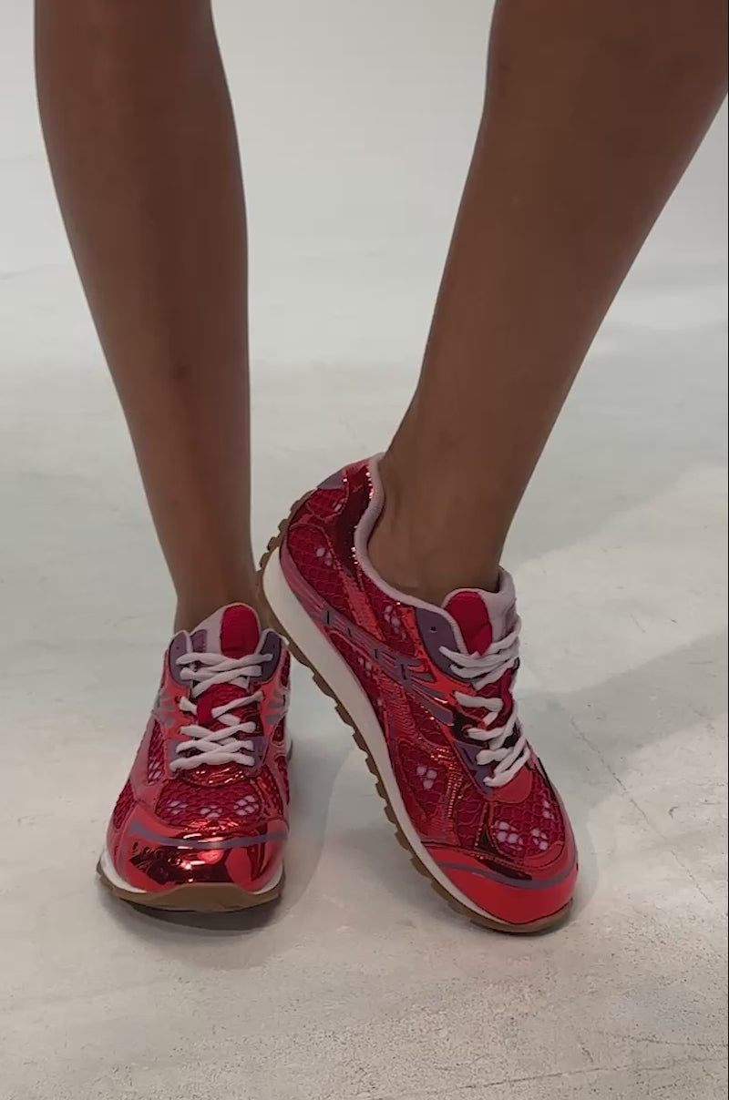 Video of woman modeling the AKIRA GOLD LENIYA RED SNEAKER—with a metallic red sporty-chic design, white laces, and brown soles