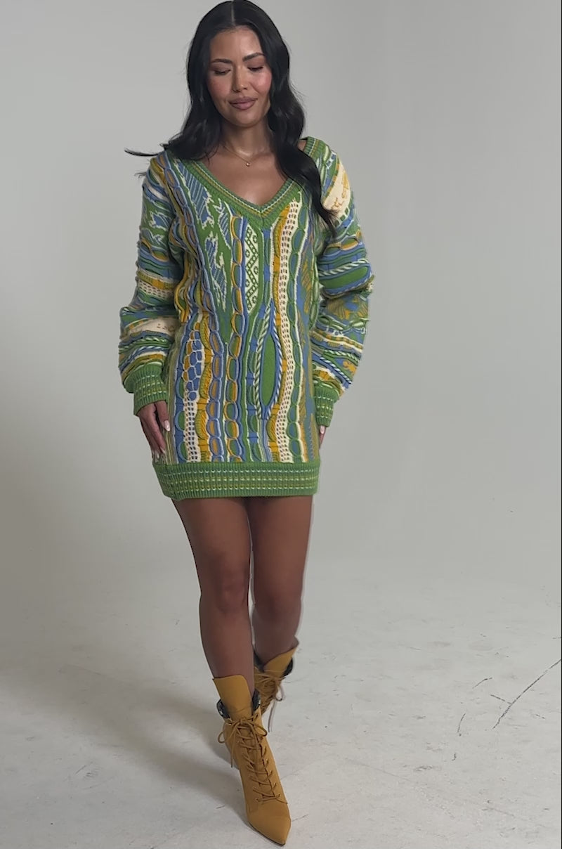 Video of woman modeling the FEELIN COZY V-NECK SWEATER DRESS, a multicolor knitted piece in green, blue, yellow, and white. 