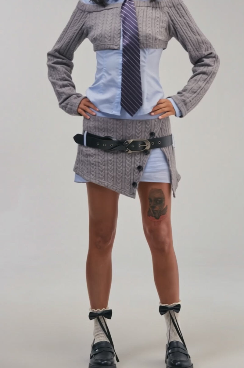 Video of a woman modeling the “CHECK IT OUT BUTTON DOWN,” layered under a gray cropped cable knit sweater.