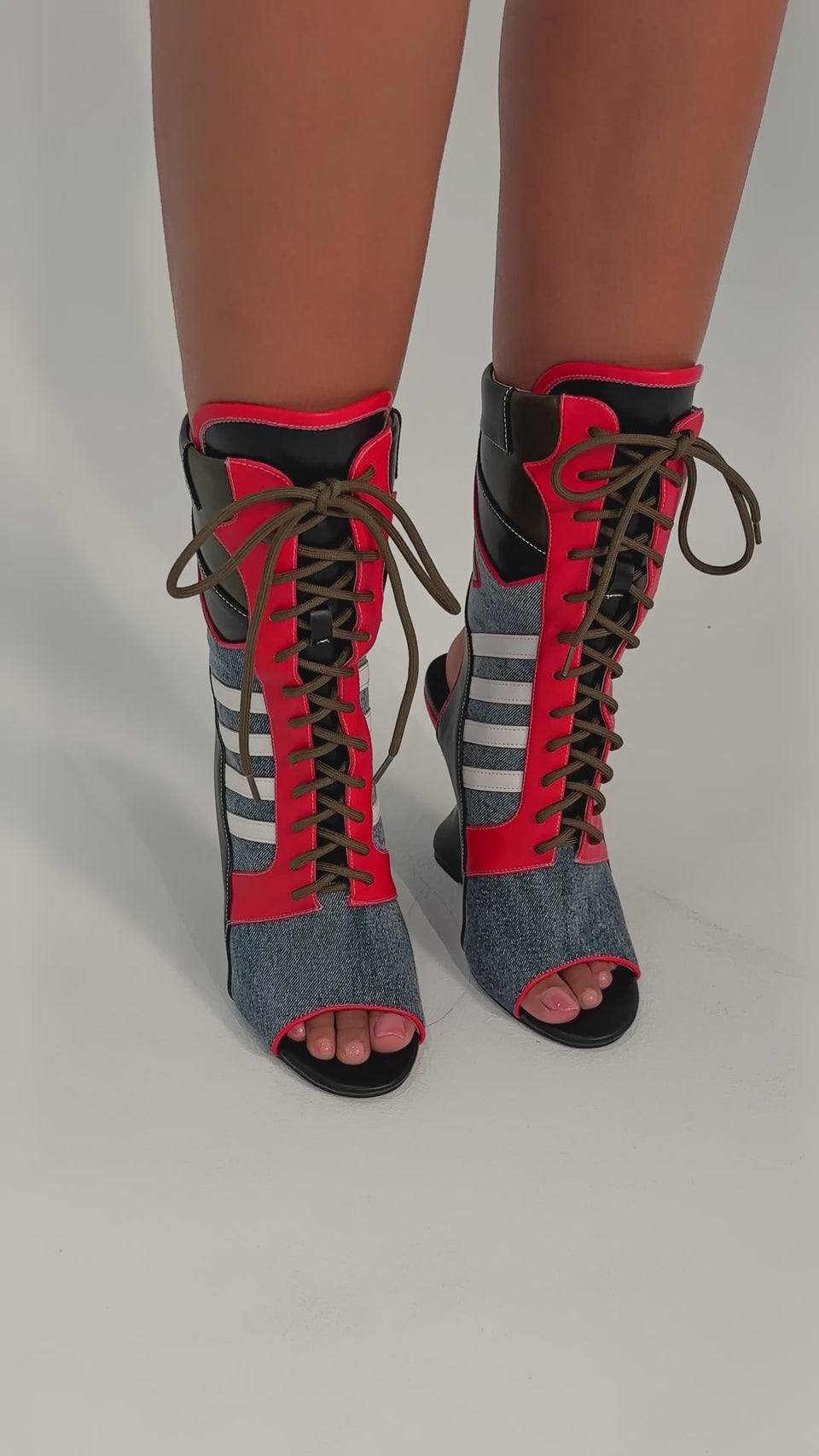 A video of a person wearing the AKIRA GOLD MAYWEATHER MULTI SPORTY LOOK WEDGE BOOTIE—open-toe, lace-up booties with denim panels in red, blue, olive green, and white stripes—while standing on a light-colored surface.