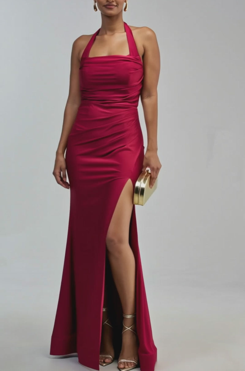 Video of a woman modeling the MYSTERIOUS MUSE HIGH SLIT MAXI DRESS—a sleeveless, floor-length burgundy gown with a halter neckline and high slit.