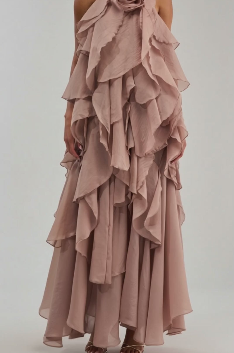 Video of woman modeling the GOLDEN HOUR FLORAL CHIFFON MAXI DRESS IN MAUVE, featuring flowing, tiered ruffles, textured chiffon layers, and a large rose detail at the neckline, set against a plain white background.