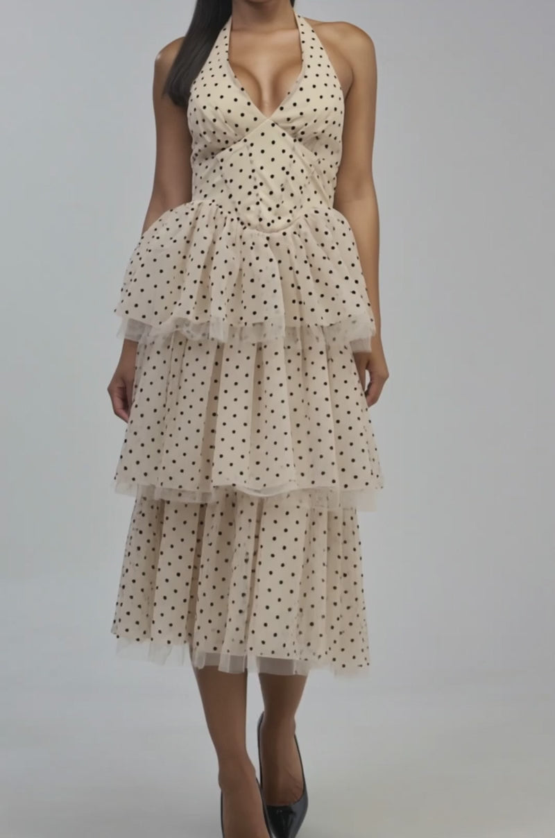 Video of a woman modeling the LOVE YOU MEAN IT POLKA DOT MIDI DRESS— a beige, polka dot halter midi dress with black spots and tiered ruffles.