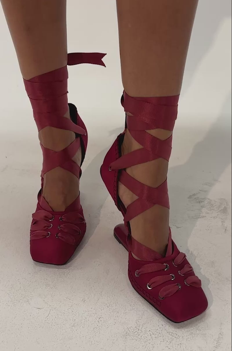 Video of a woman modeling the AZALEA WANG PIROUETTE WINE WEDGE PUMP, featuring wine red satin and ribbon ties wrapped around their ankles.