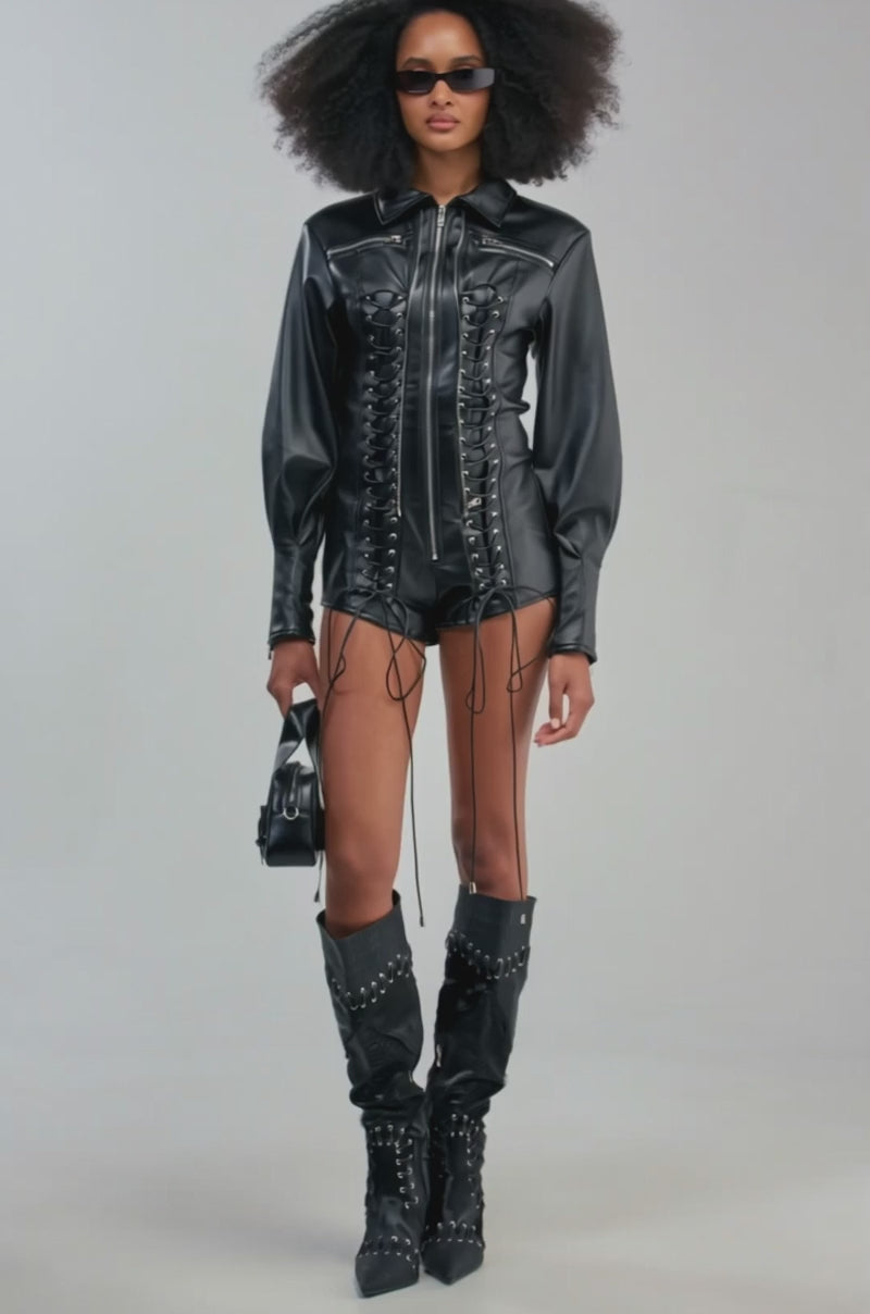 Video of a woman modeling the AT THE MAIN STAGE PU ROMPER—a black faux leather lace-up romper featuring long sleeves and front zippers.