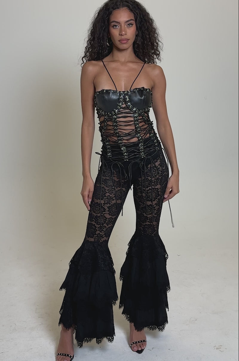 Video of woman modeling the TIE ME UP LACE UP CORSET in black faux leather paired with black lace pants, standing against a plain light grey background for a chic, waist-sculpting look.