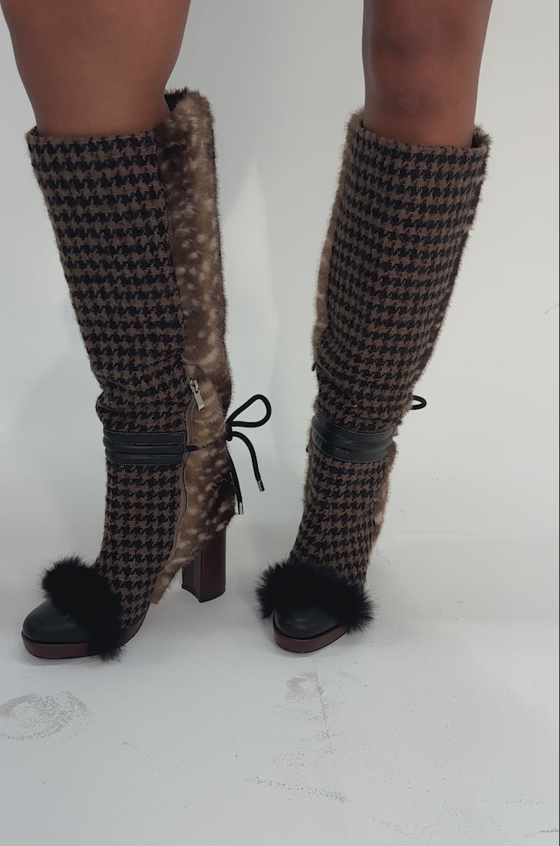 Video of woman modeling the AKIRA GOLD MIKAELA BROWN MULTI MATERIAL BOOT, featuring knee-high faux fur, chunky heels, houndstooth patterns, black ribbon ties at the back, and playful black pom-pom accents at the toes.